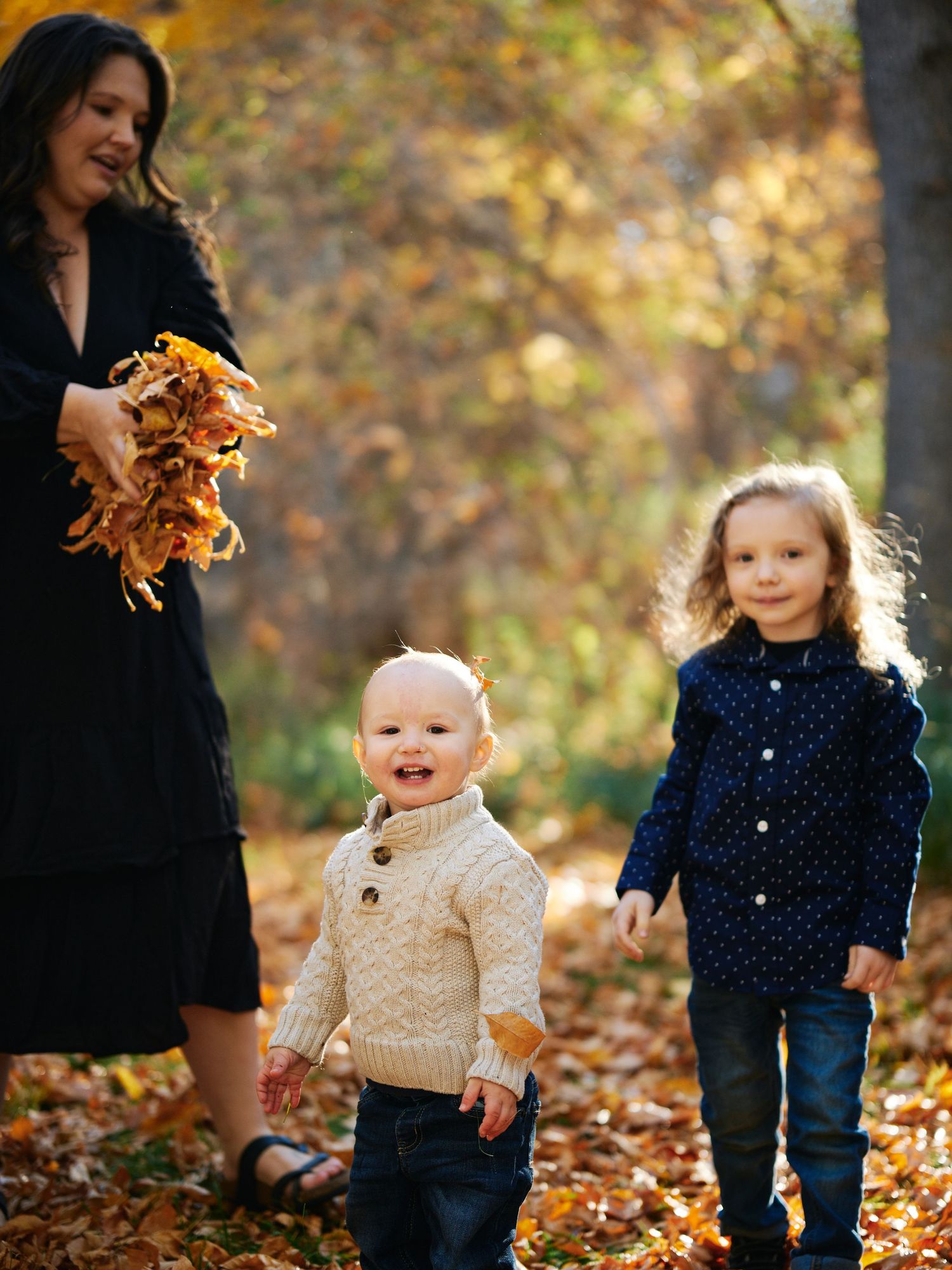 Three figures play with autumn leaves on a sunny fall afternoon.