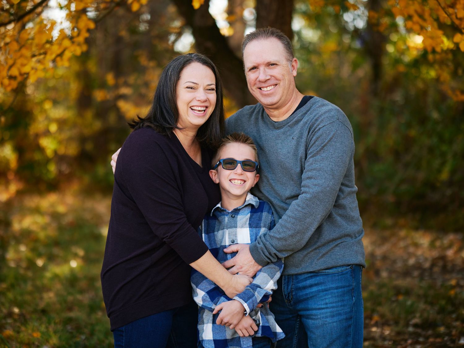 A family group embraces while standing against autumn foliage.