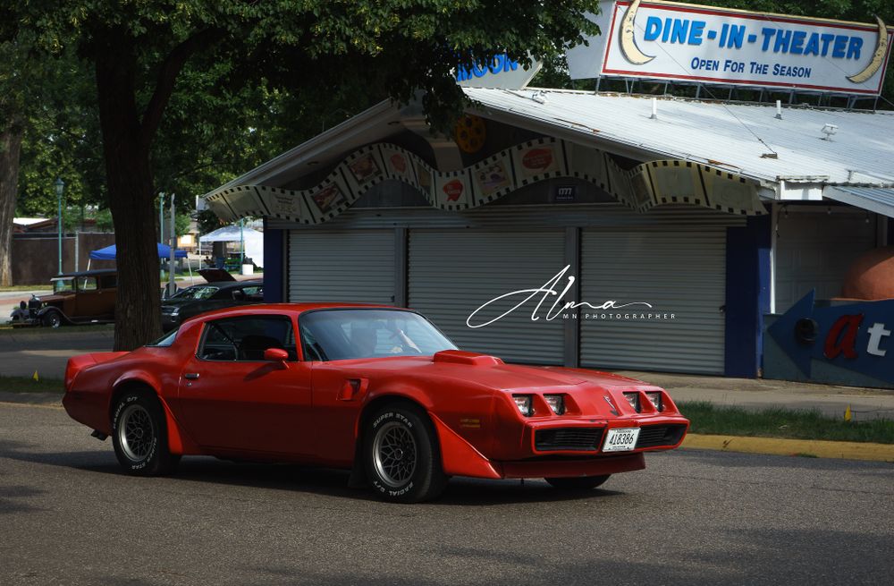 Classic red Pontiac Trans Am parked in front of a vintage drive-in theater.
