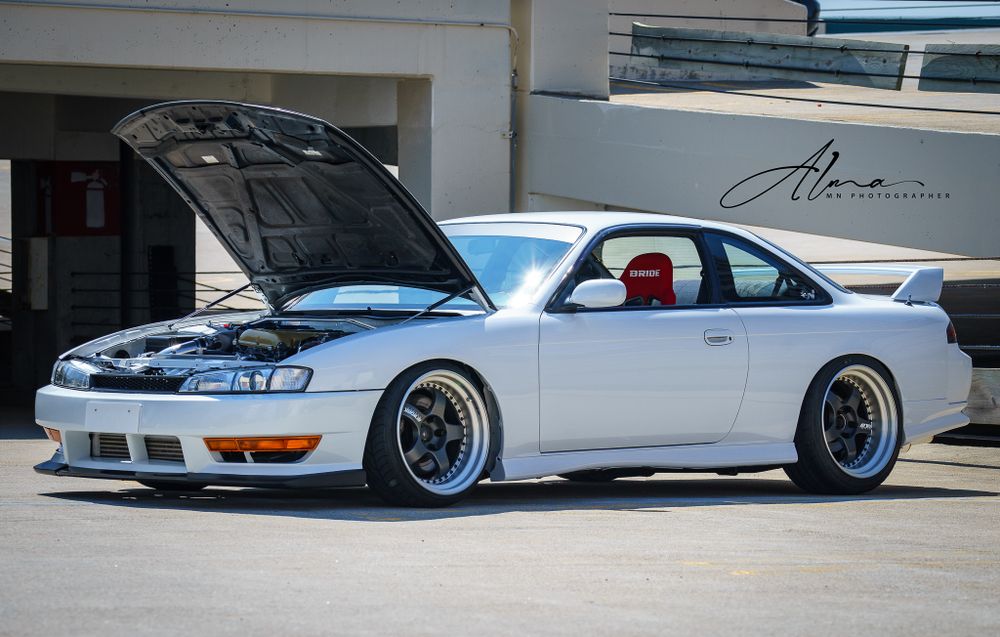 Modified white Nissan Silvia S14 with wide body kit and custom wheels.