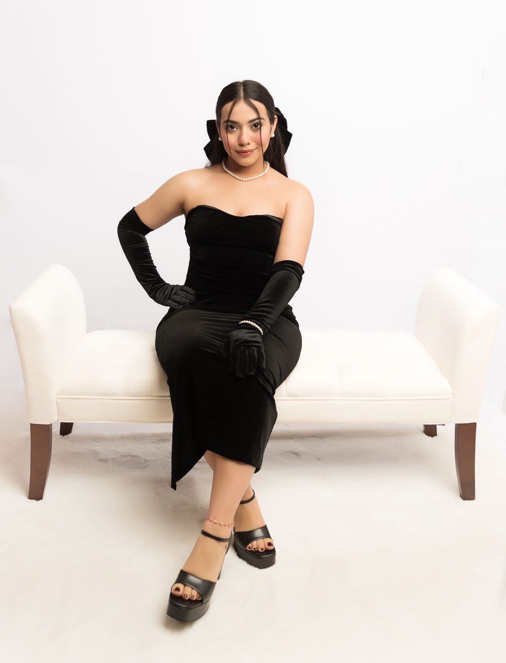 Classic glamour pose on white bench wearing black velvet evening dress and gloves.