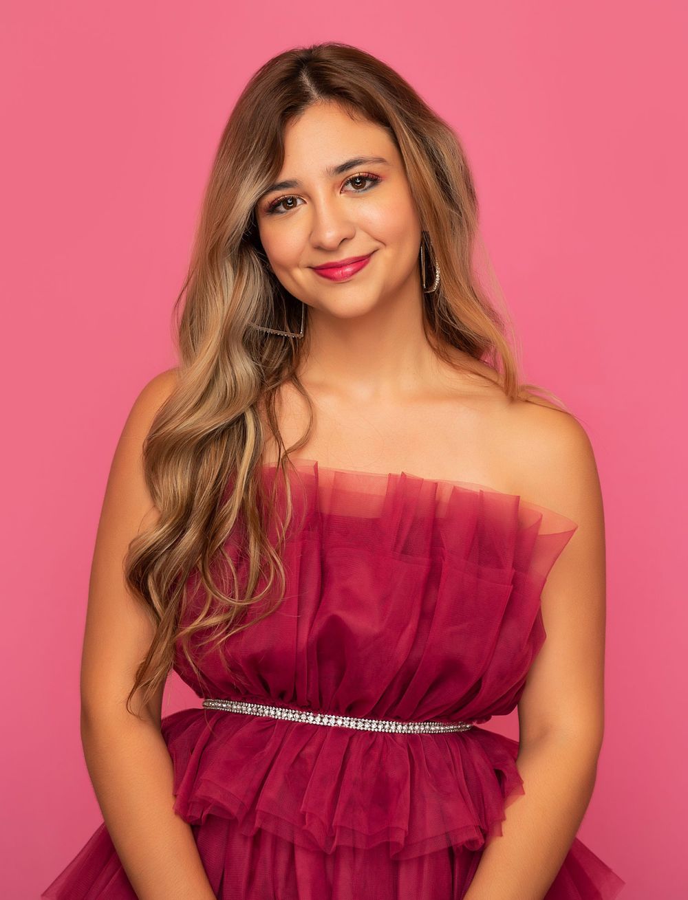 Close-up portrait featuring a magenta tulle dress with rhinestone belt against pink background.