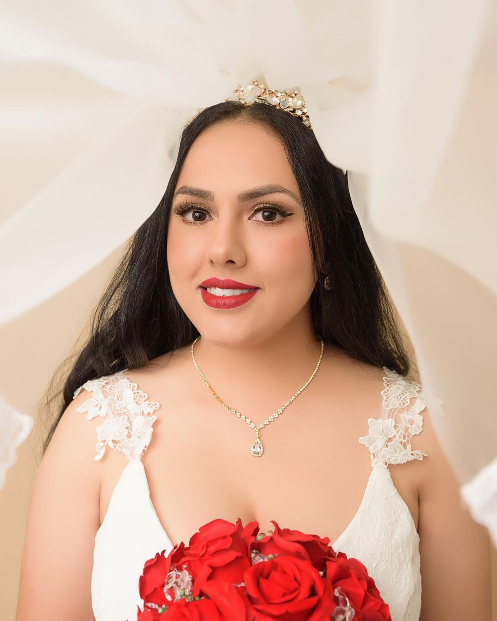 Portrait in bridal attire with crystal crown and red rose bouquet against white background.