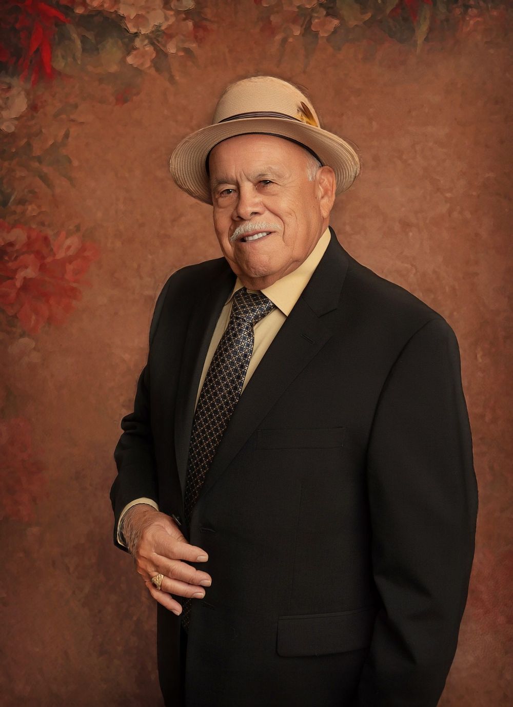 Portrait of gentleman in suit and fedora against textured brown backdrop with foliage.