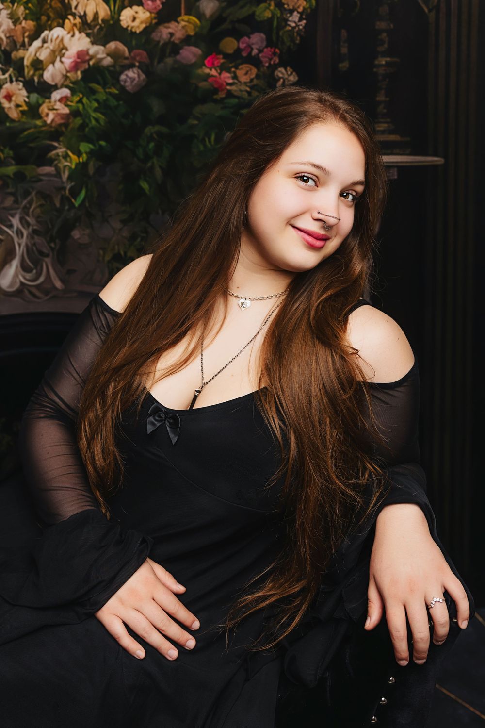 Woman in black dress smiles warmly against backdrop of pink roses and dark decor.