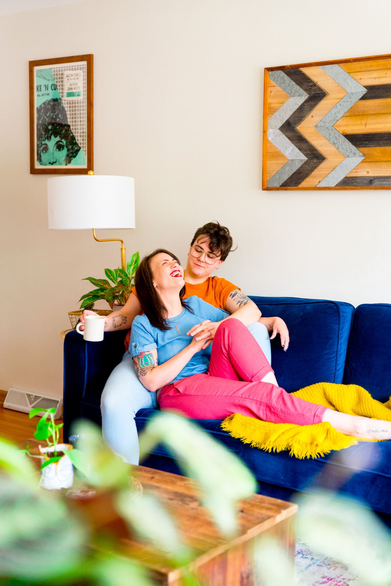 woman in pink pants laughing and cuddling with woman in orange shirt on blue couch in their Chicago apartment