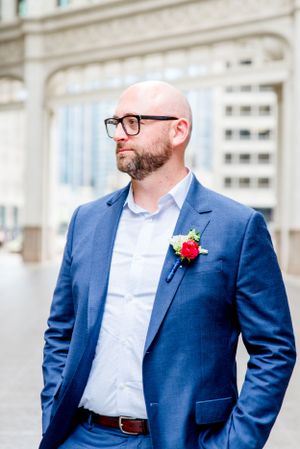 man in navy suit and glasses standing under Wrigley Building Chicago