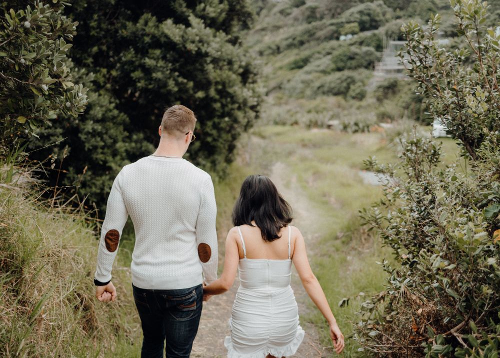 A couple walking hand in hand along a nature trail surrounded by green foliage and hillside.