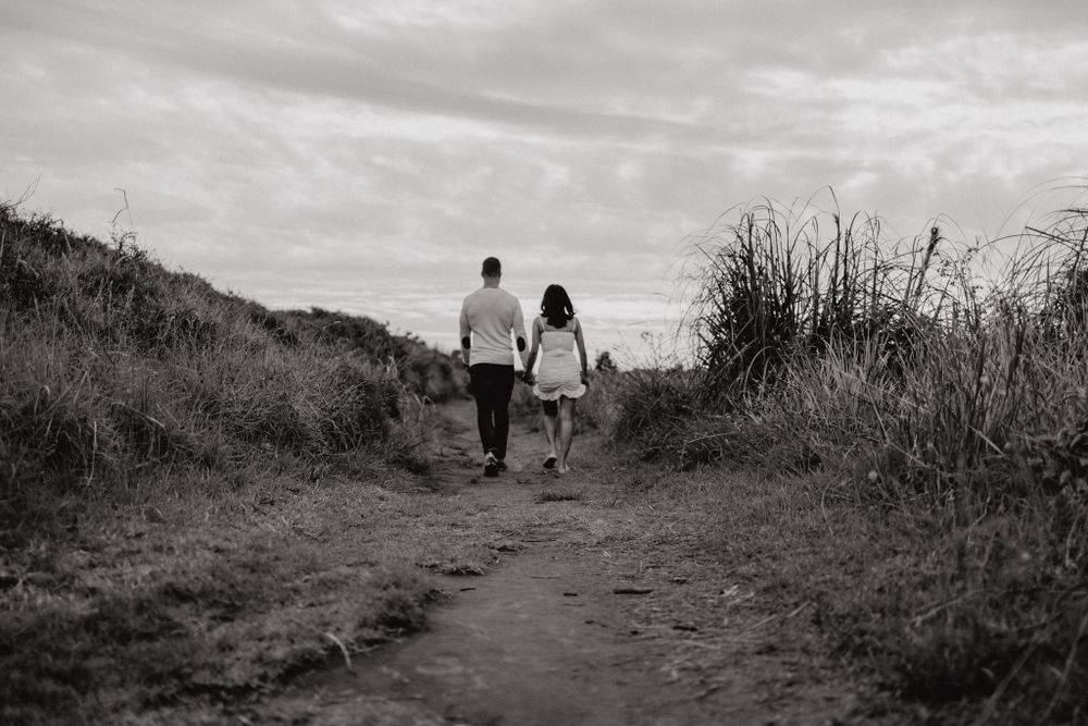 Black and white photo of two people walking on a dirt path through grassy hills.