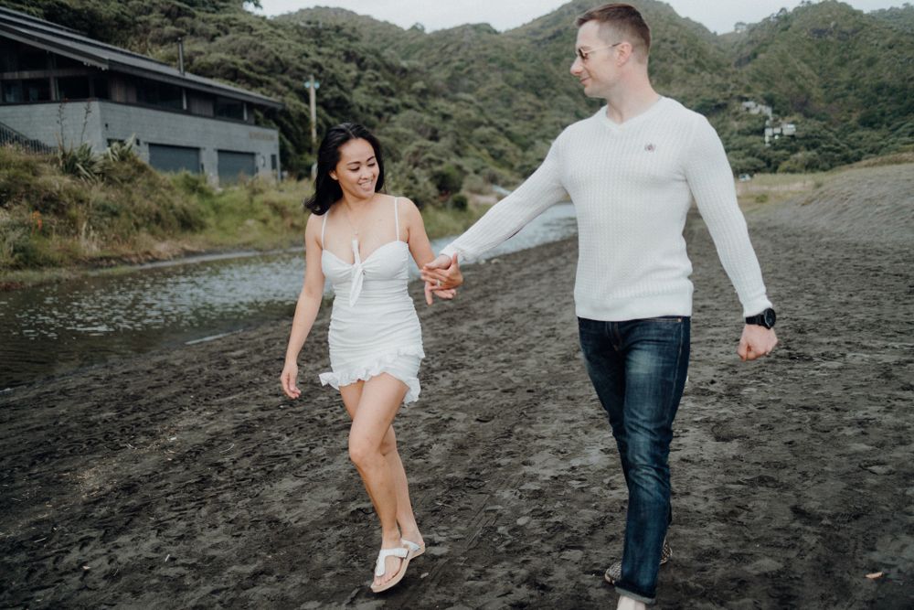 A couple strolling together on a black sand beach with mountains in the background.
