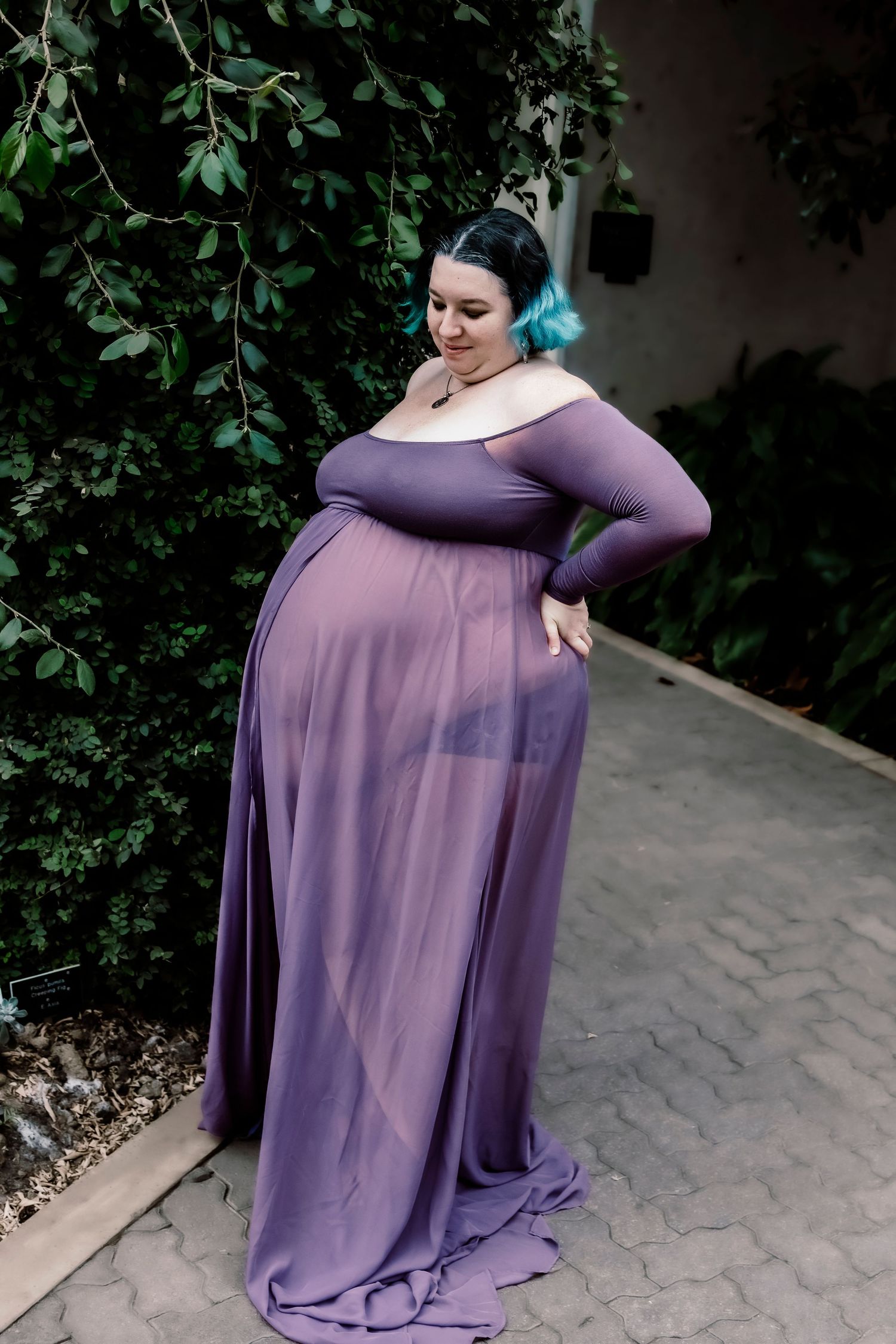 A flowing purple maternity dress photographed in an elegant garden setting.