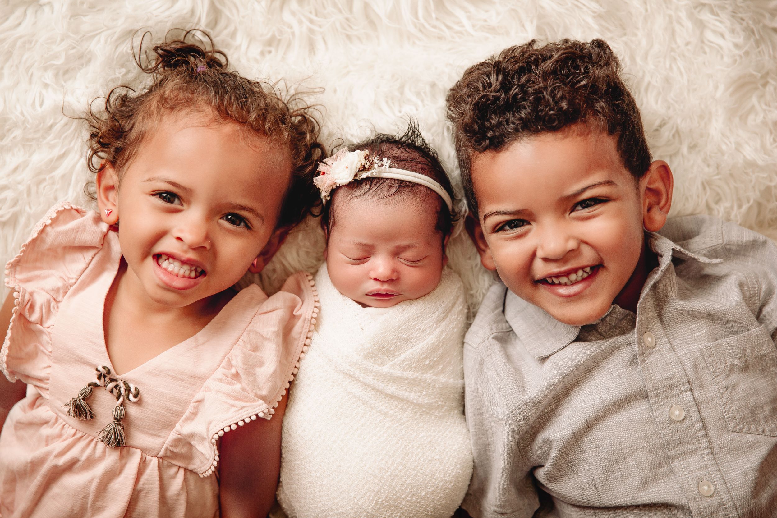 newborn baby and 2 children laying on white flokati fur