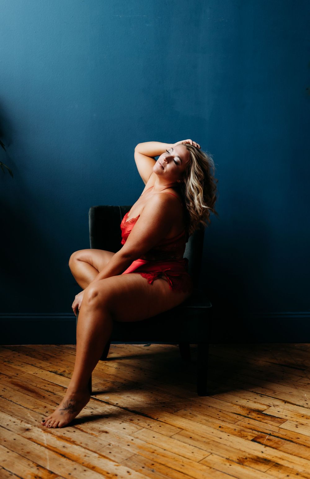 Atmospheric photo with dramatic lighting showing a red lingerie pose on dark chair.