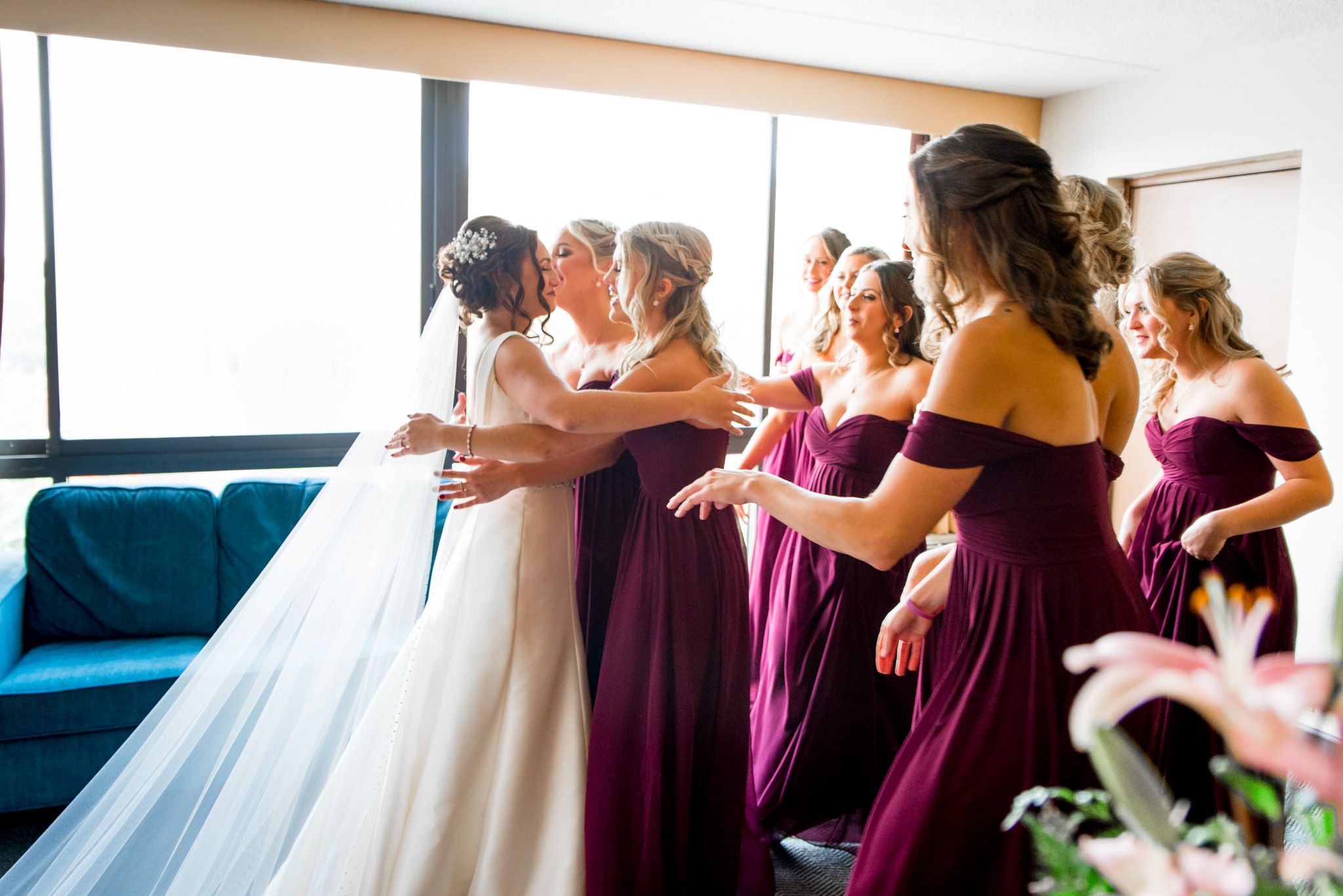 bridesmaids embrace the bride wearing her white wedding dress and veil