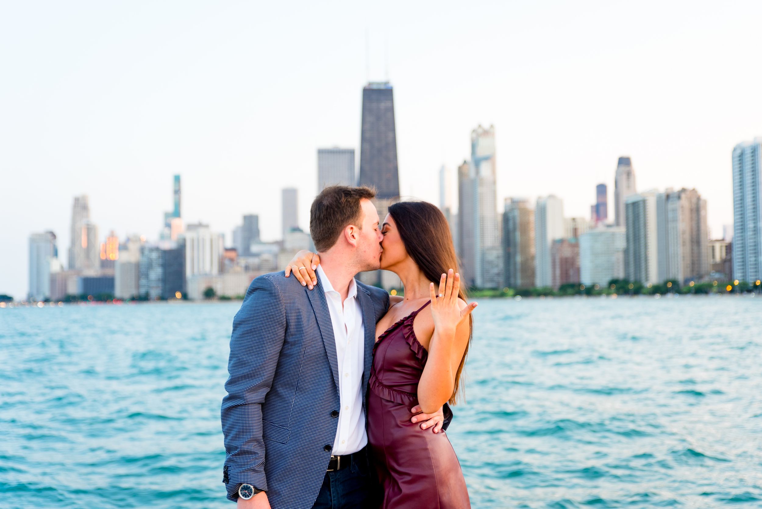 man and woman kissing and woman holding up hand in front of skyline after Chicago Proposal