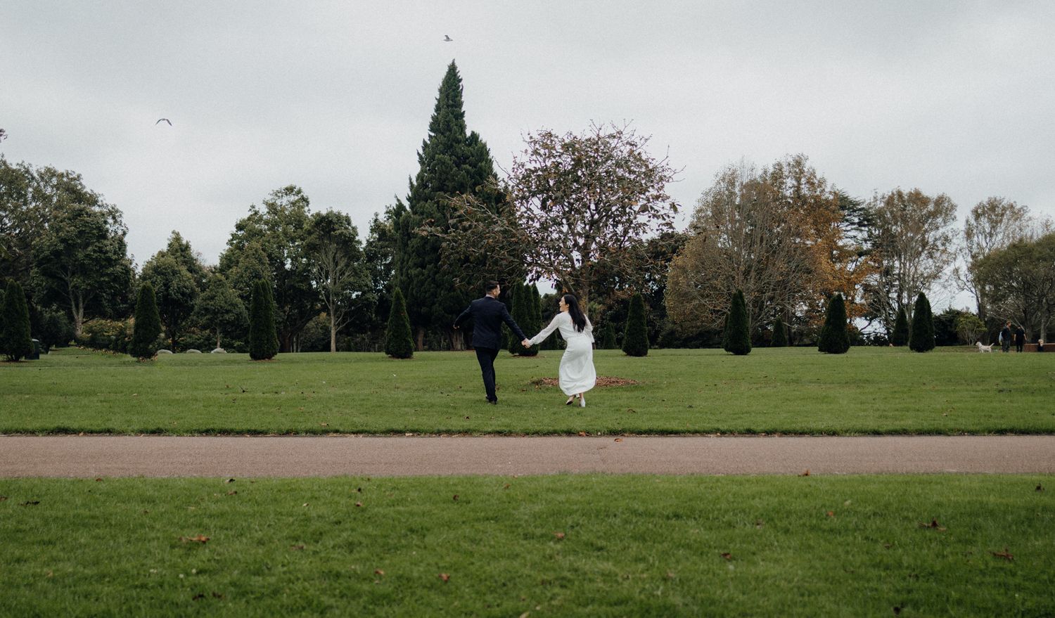 Dancing newlyweds in a park with green grass and evergreen trees in the background.