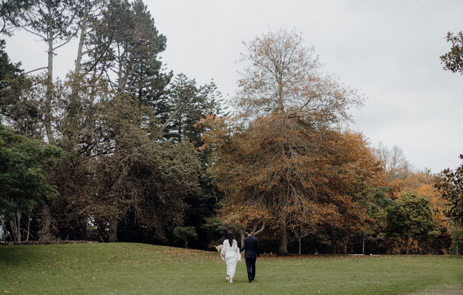 A couple stands beneath autumn trees in a peaceful park setting.