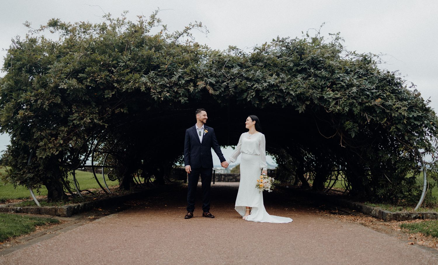 Couple standing under an archway of green foliage.