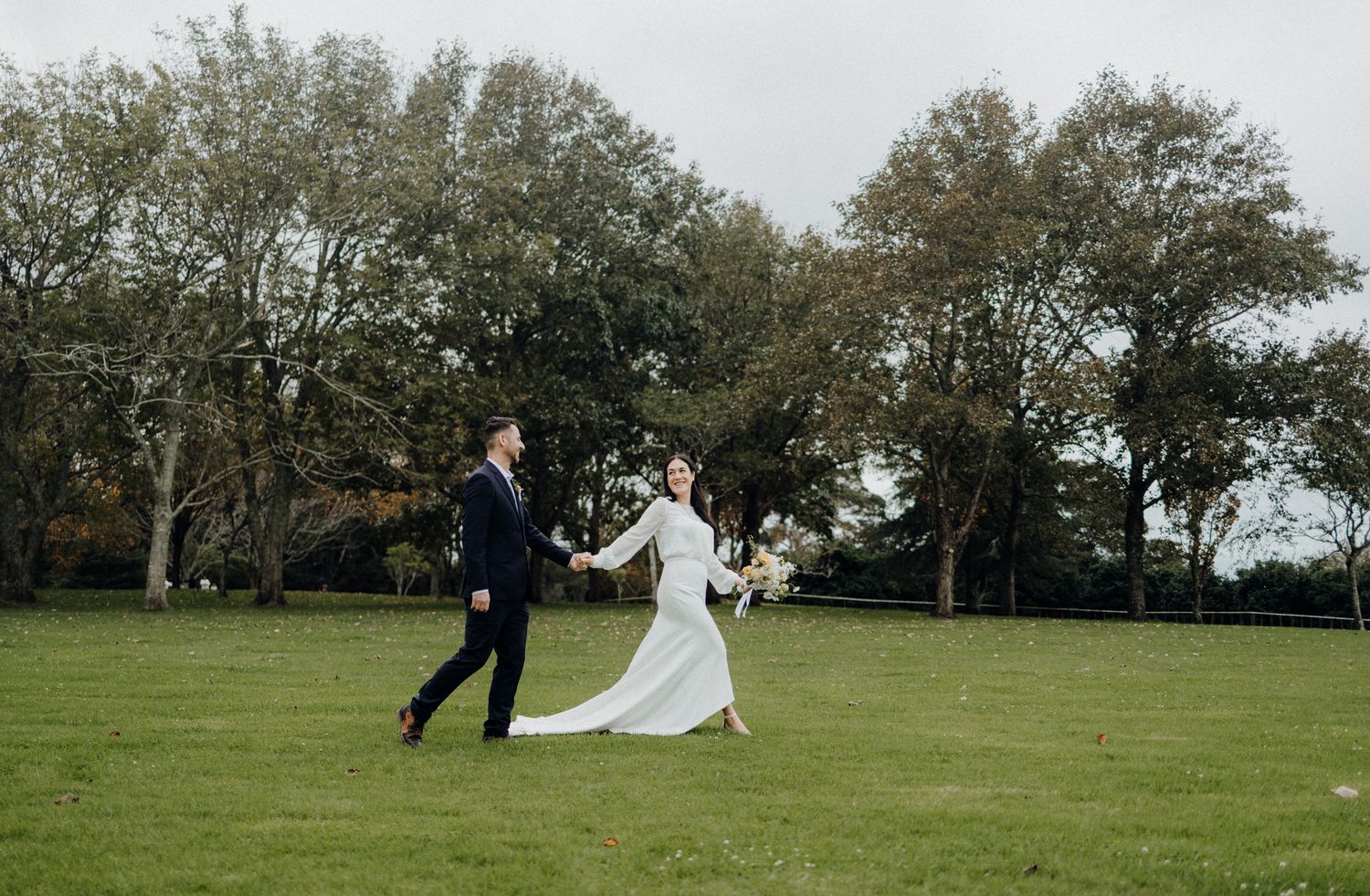 Couple running playfully across a grassy field.