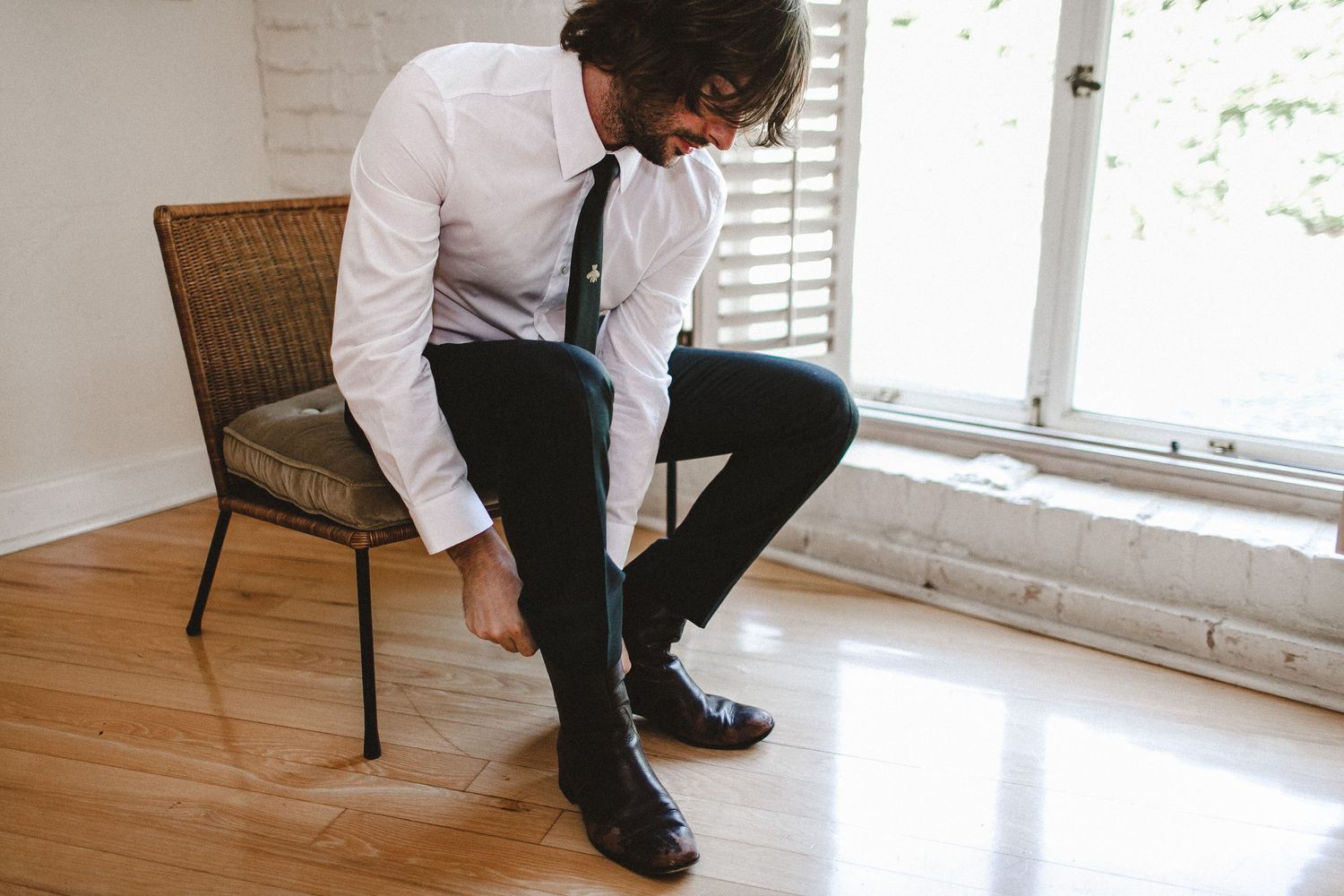 groom putting on shoes sitting next to window