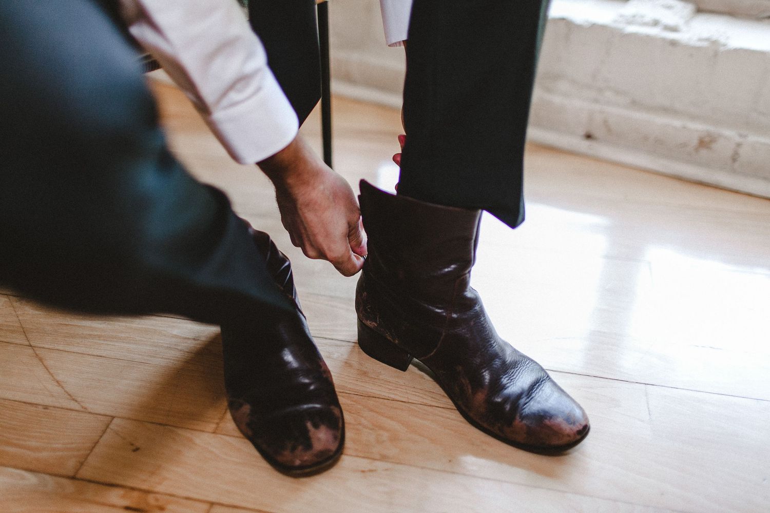 close photo of groom putting on boots for wedding day