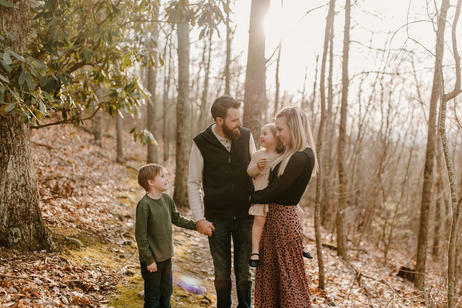 Family of three standing together on an autumn forest trail during golden hour.