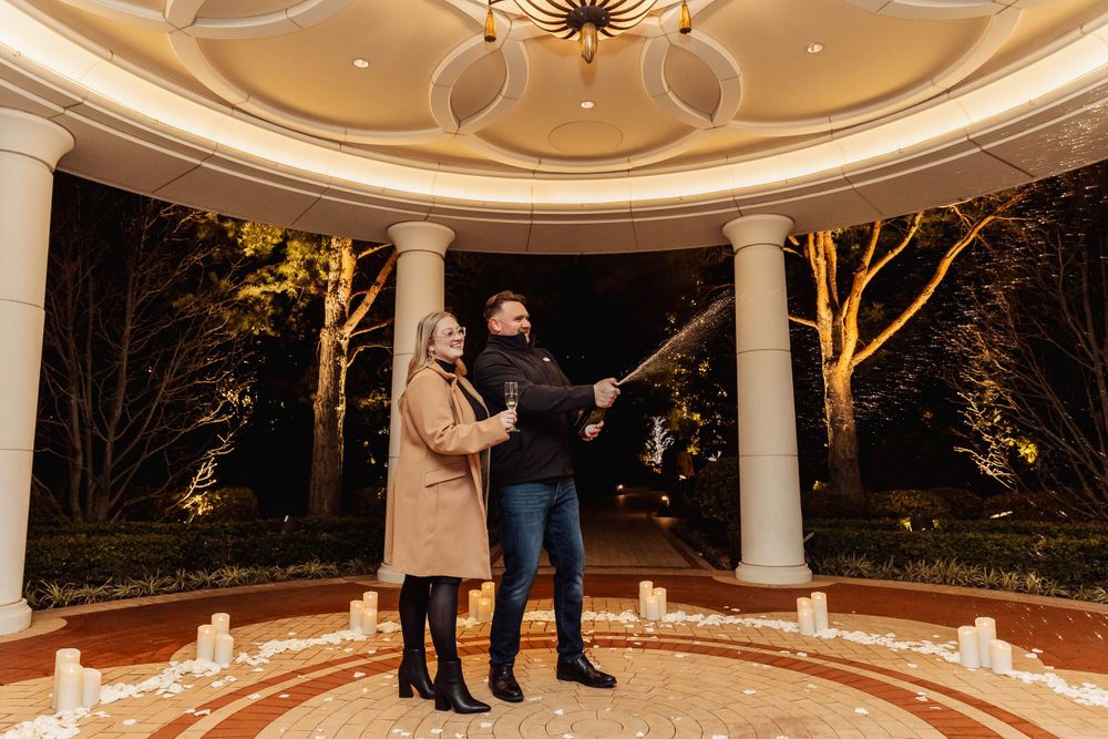 A couple sharing a joyful moment in an illuminated gazebo surrounded by trees.