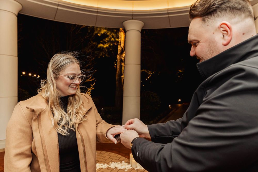 Close up of an engagement ring exchange under a gazebo lit by string lights.