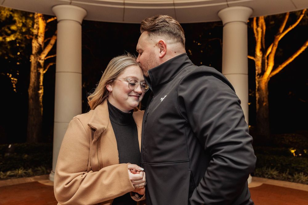 Couple sharing an intimate moment in a gazebo at night with romantic lighting.