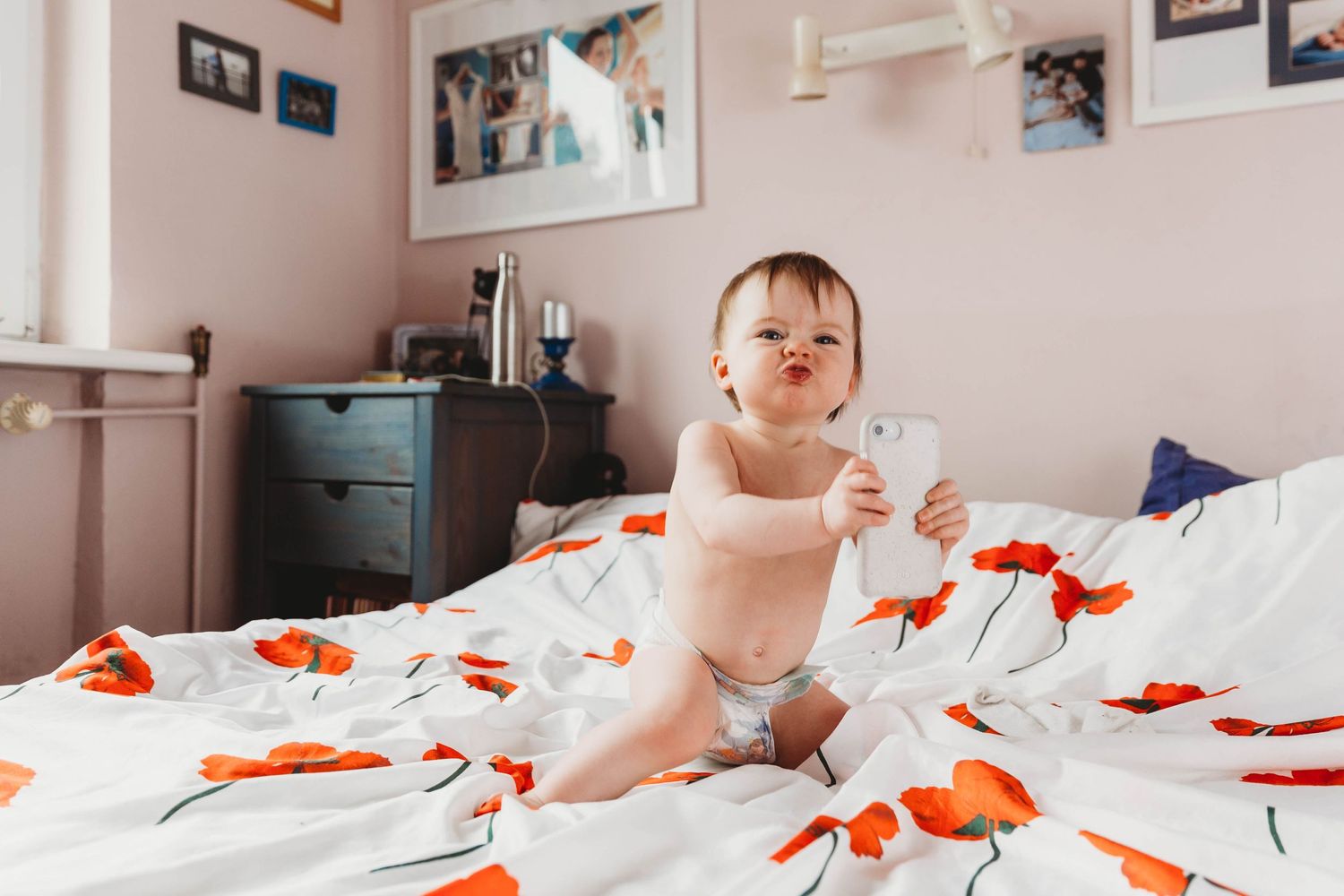 little girl in nappy holding mobile phone sitting on bed