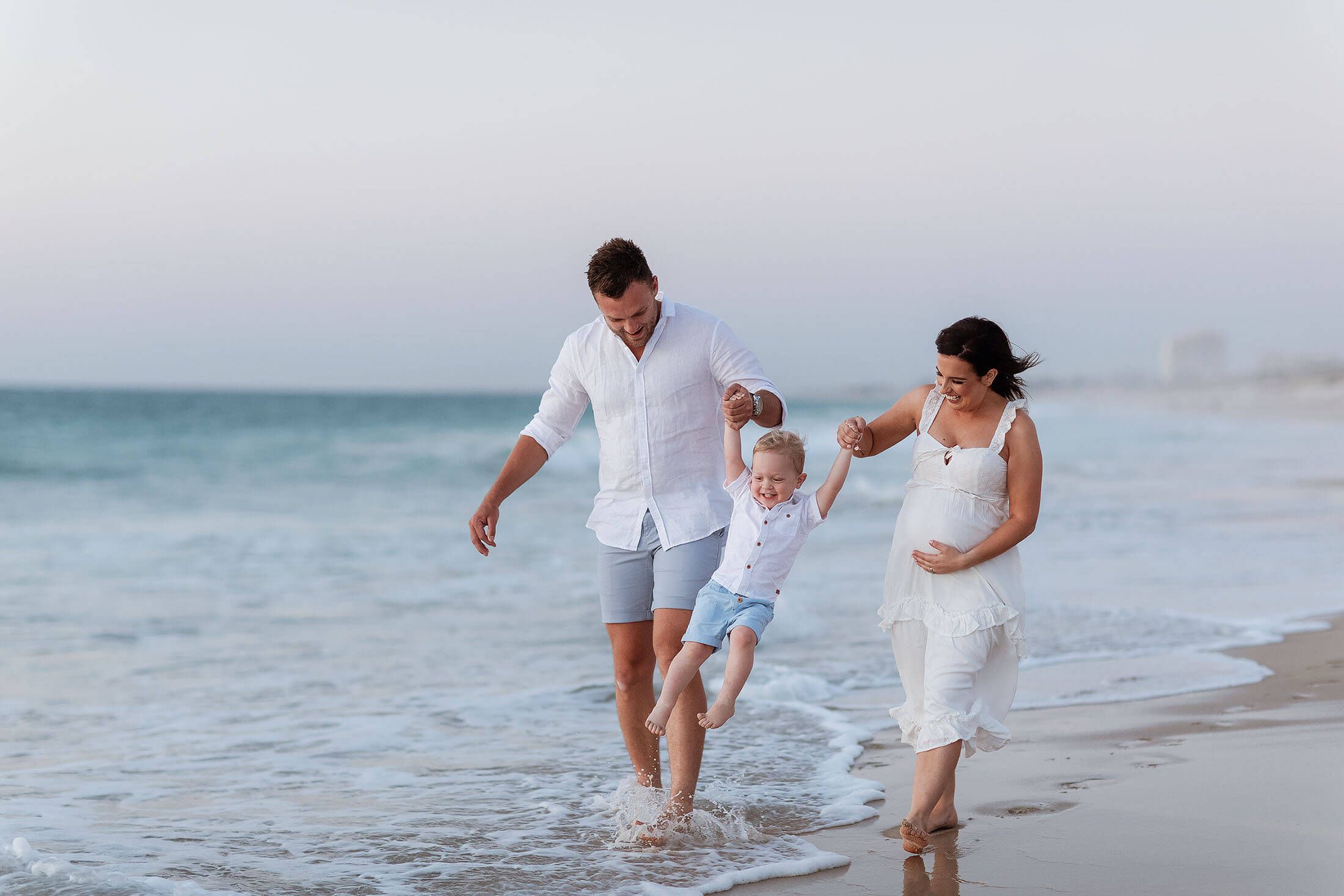 A family walking along the beach swinging their young son at sunset in Perth, Western Australia