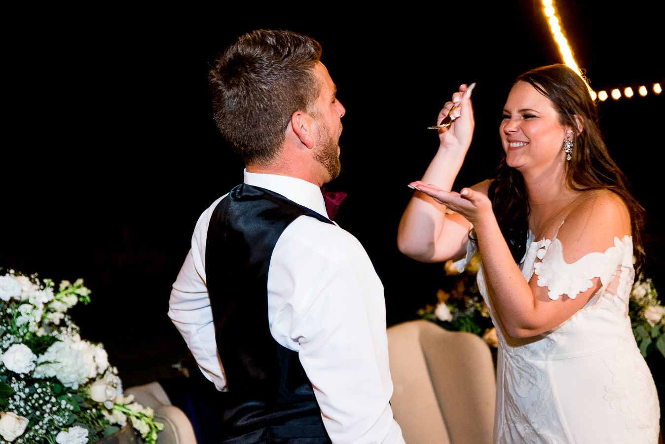bride smiles at groom and feeds him wedding cake
