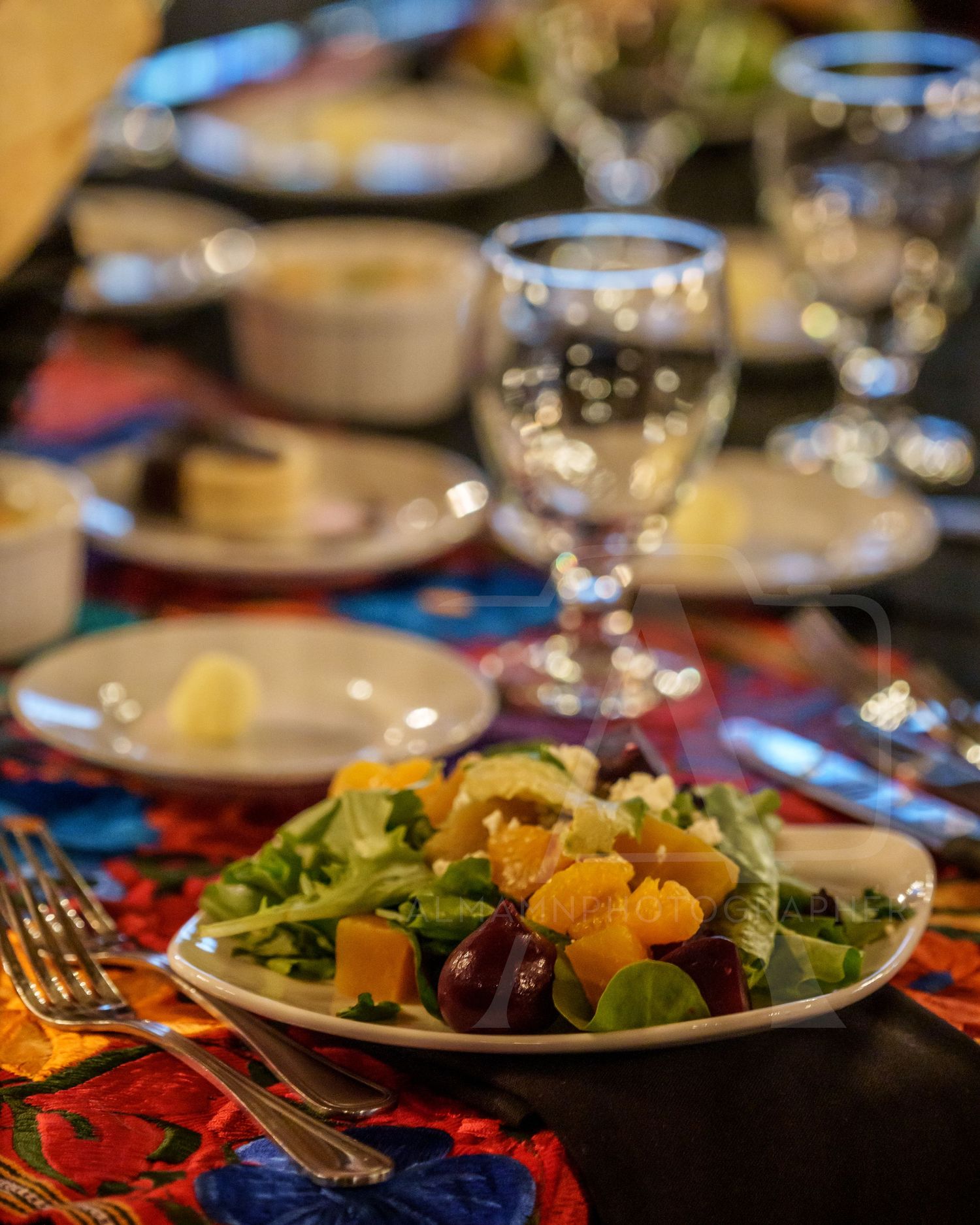 Elegant place setting with colorful salad and wine glass on patterned tablecloth.