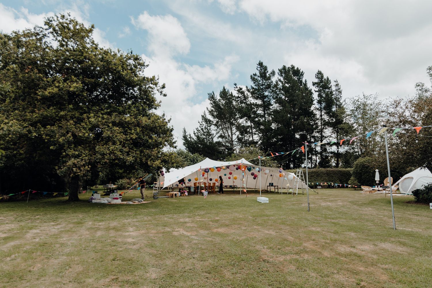 Outdoor wedding venue with white tents set up on green lawn surrounded by trees.