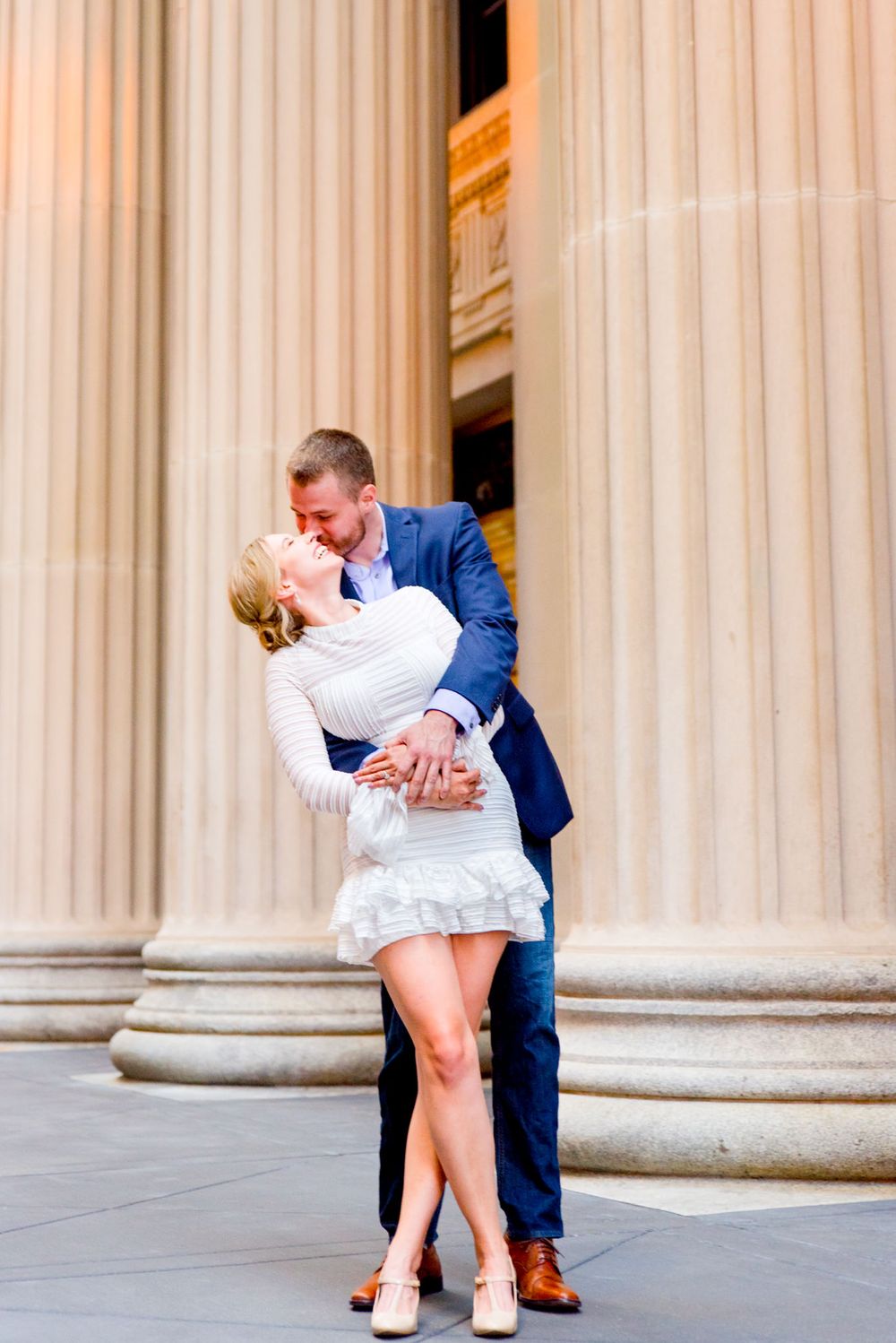 man kissing woman in white dress laughing at Chicago Board of Trade engagement pictures downtown Chicago sunset