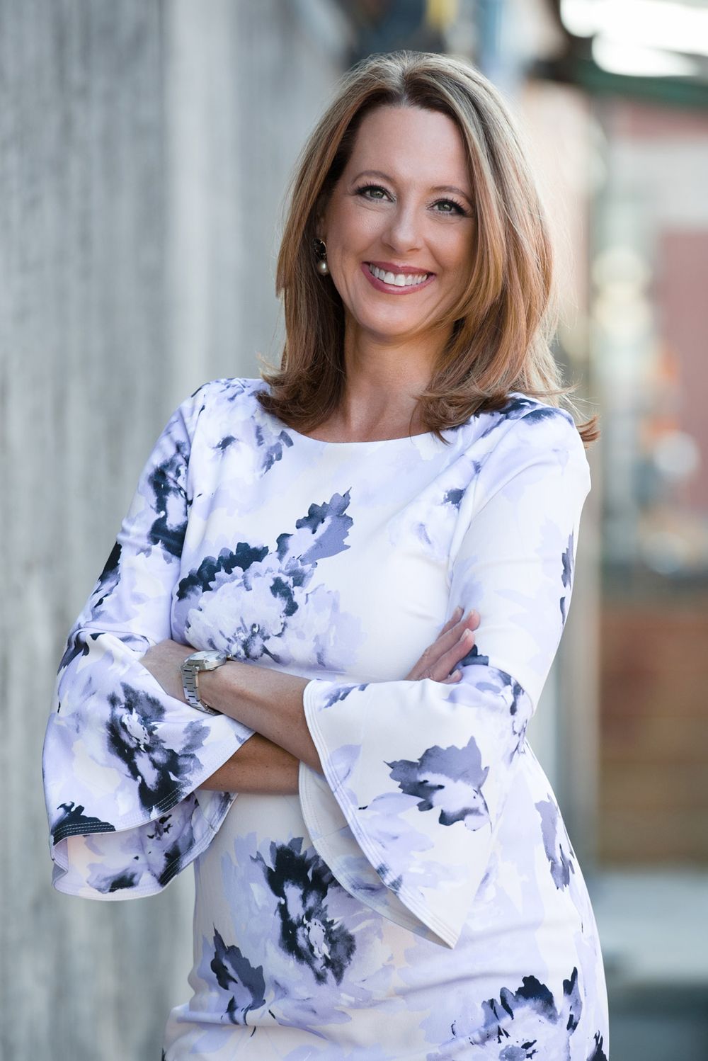 Professional portrait of woman in floral print top with bell sleeves against urban background.