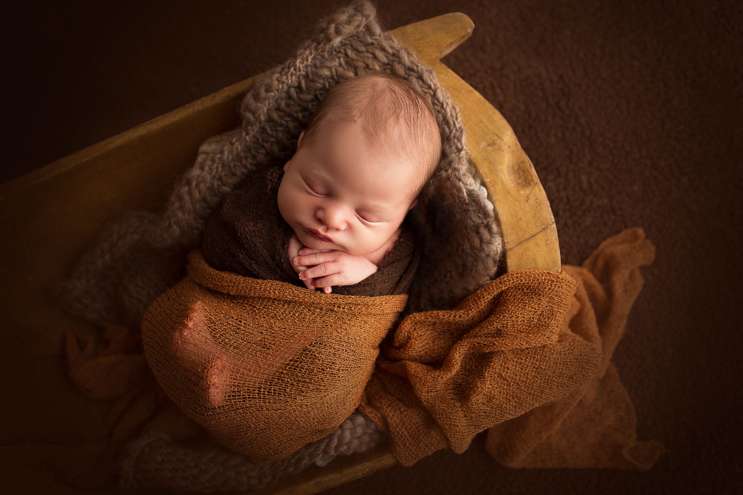 sleeping newborn boy wrapped in brown blanket in bowl
