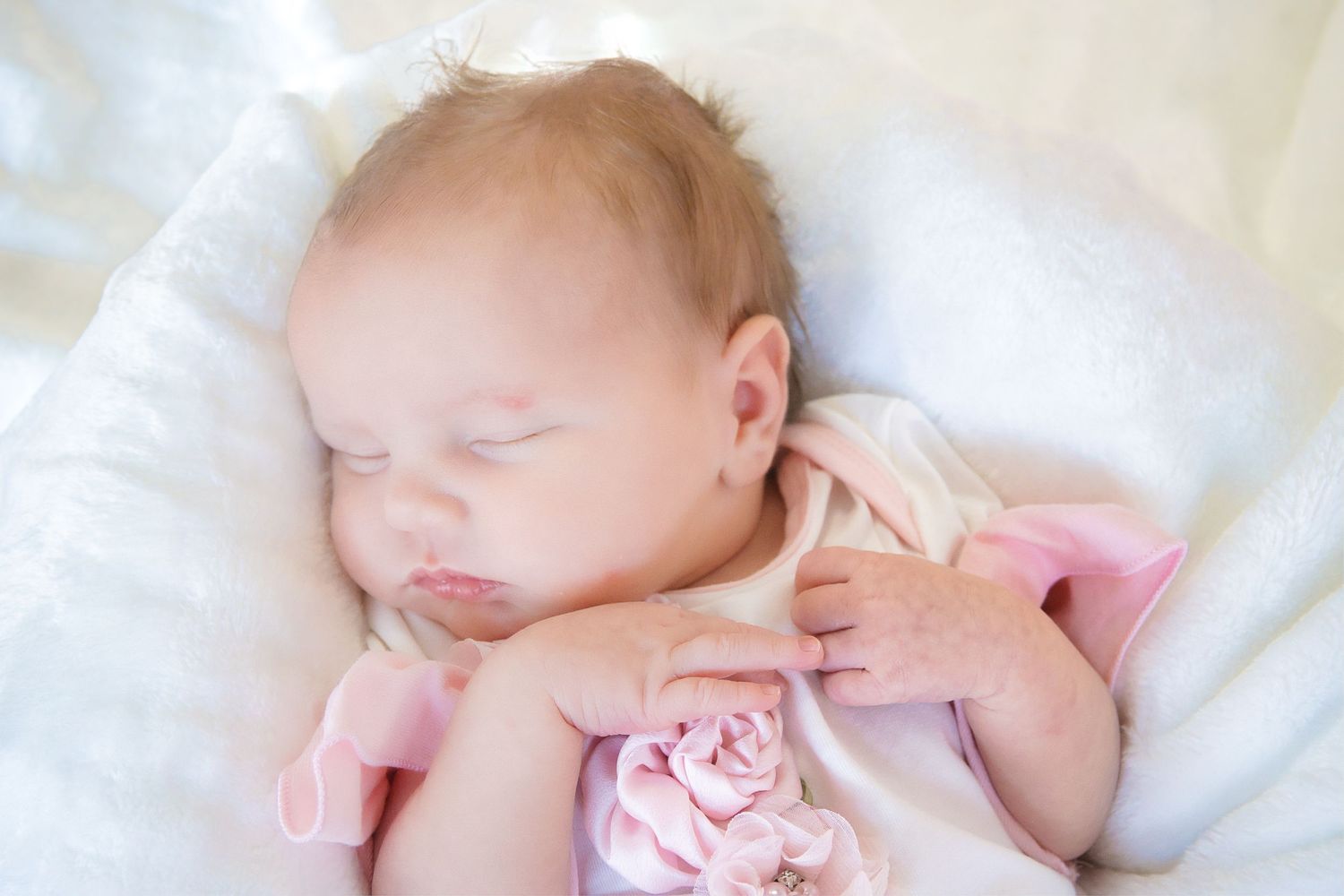 Baby sleeping peacefully on white bedding wearing pink clothing.