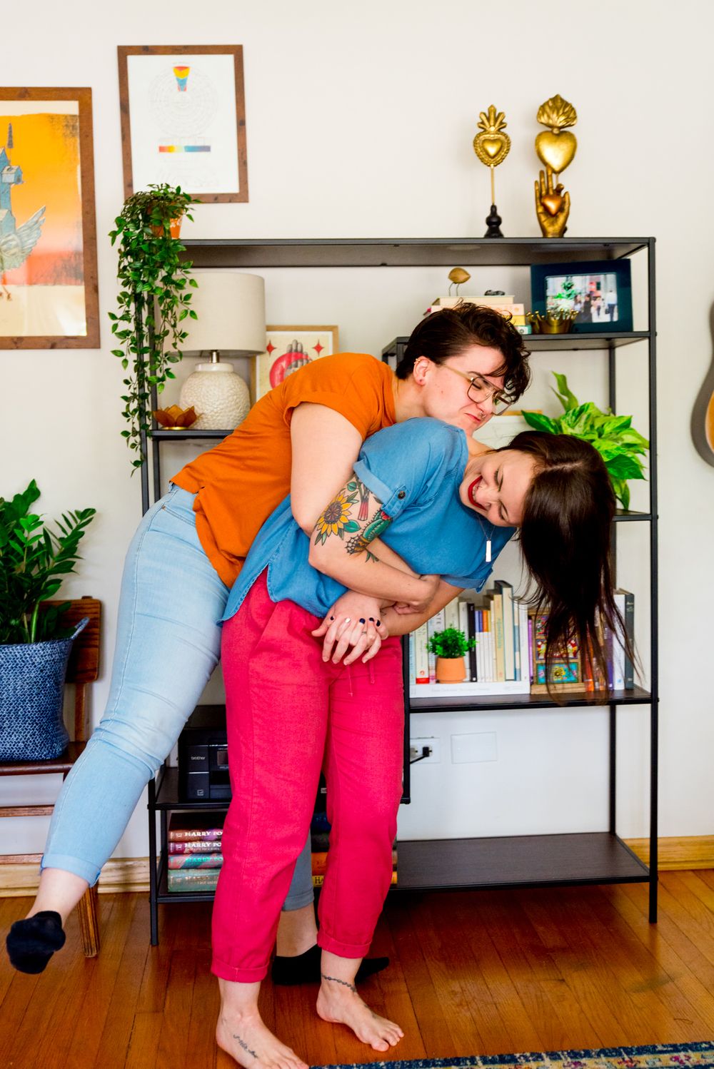 woman in orange shirt hugging woman in blue shirt bending over laughing