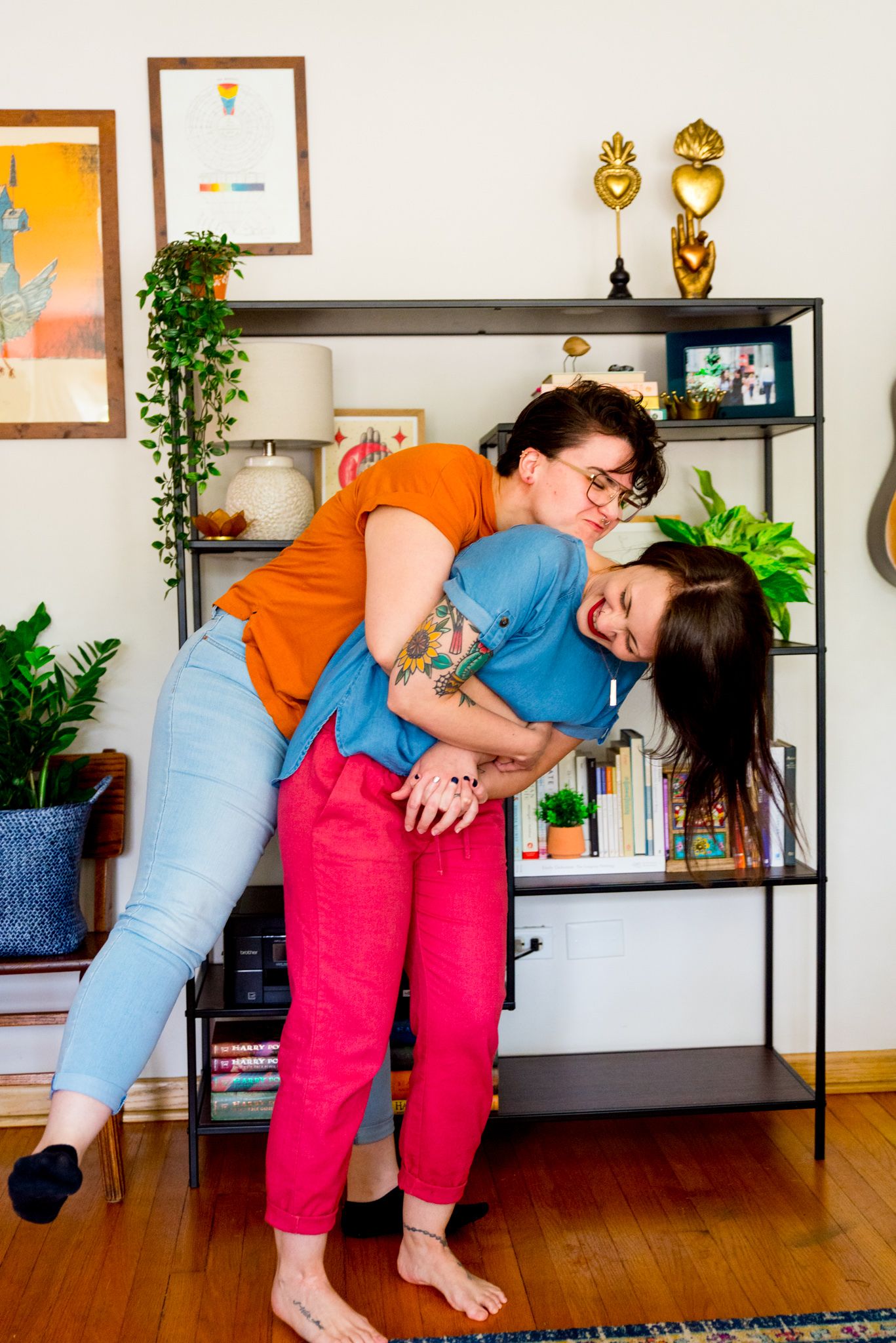 woman in orange shirt hugging woman in blue shirt bending over laughing