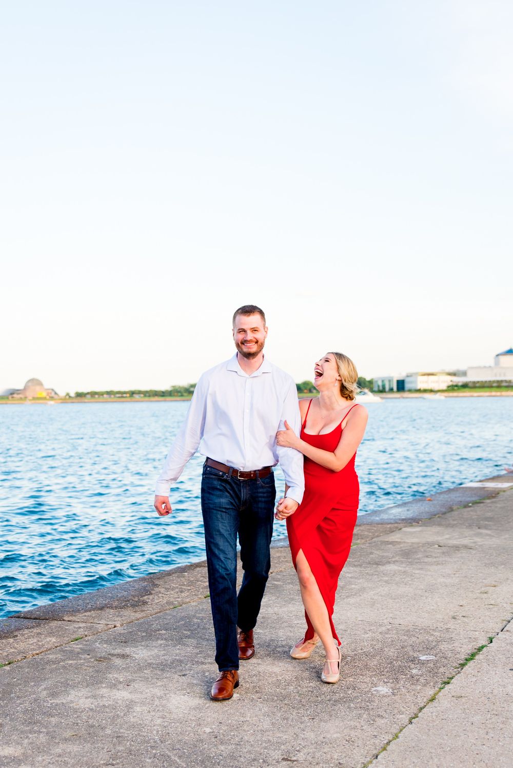 woman in red dress laughing with her fiance next to Lake Michigan