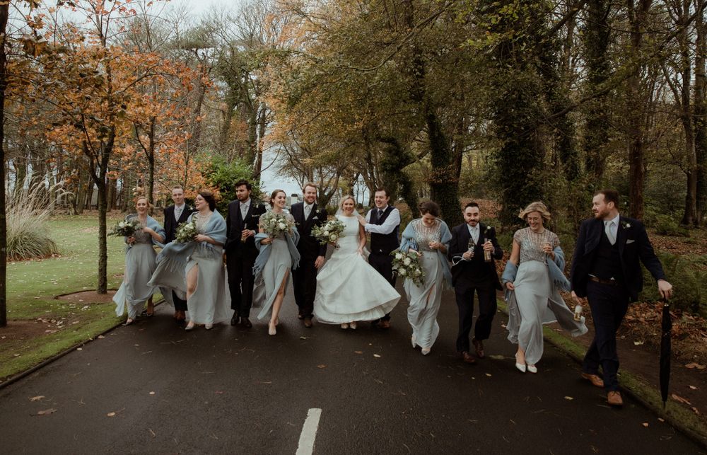 large bridal party having fun as they walk down down a path with autumnal trees