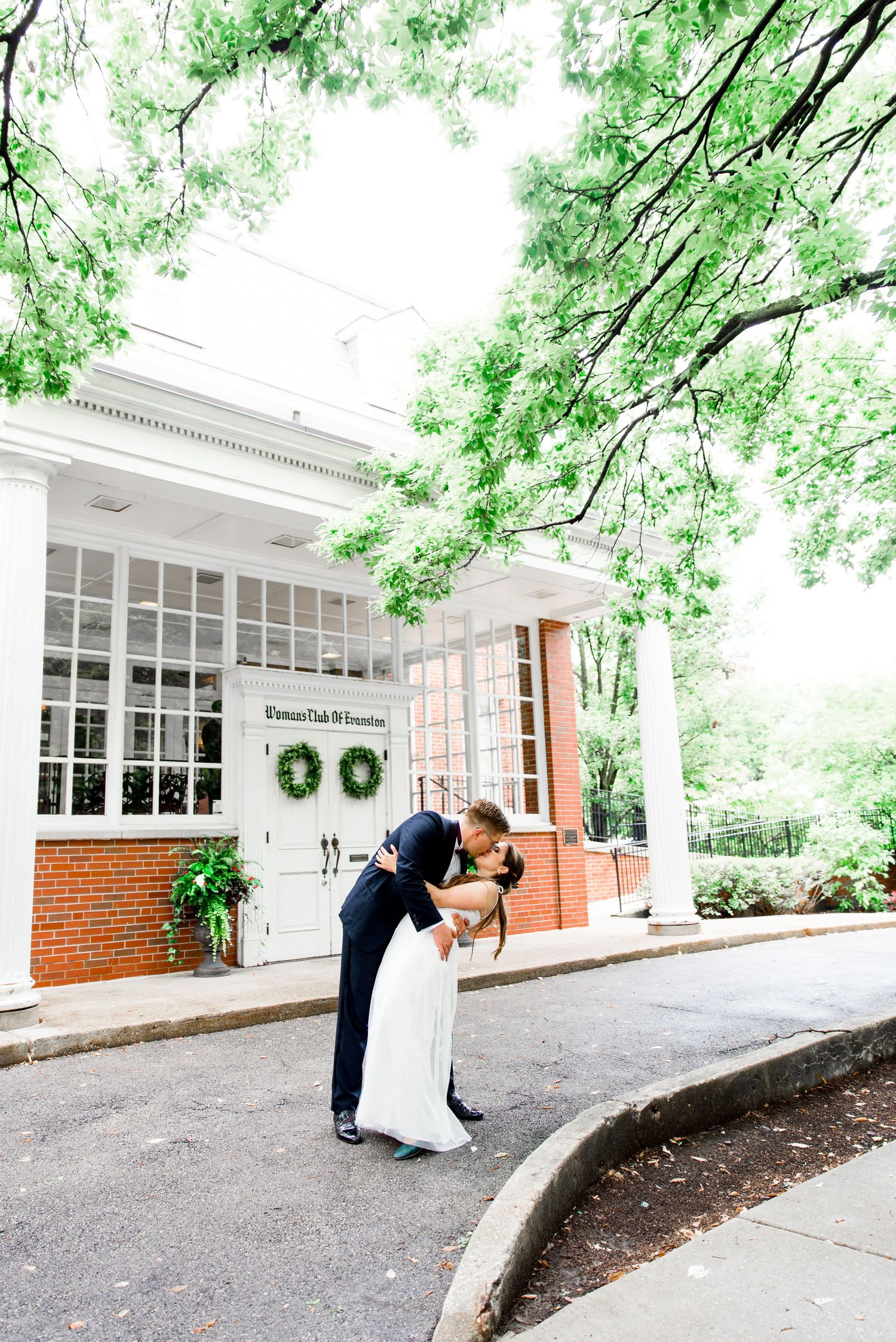 bride and groom kiss and dip in the middle of a rainy street in front of the Woman's Club of Evanston
