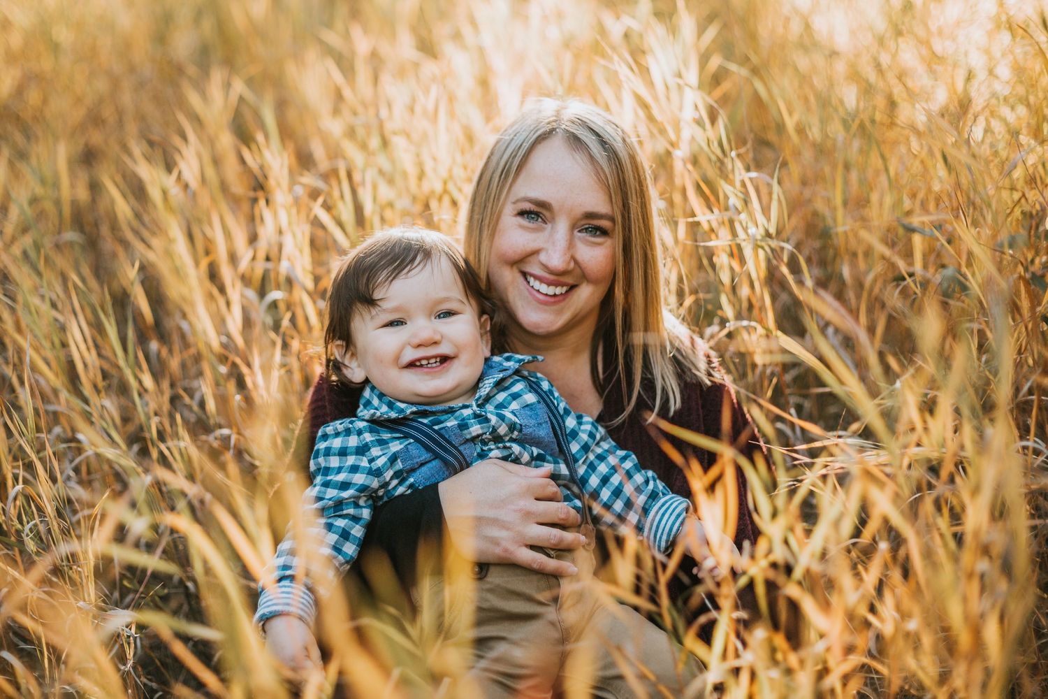 Mom and son sit in a field smiling.