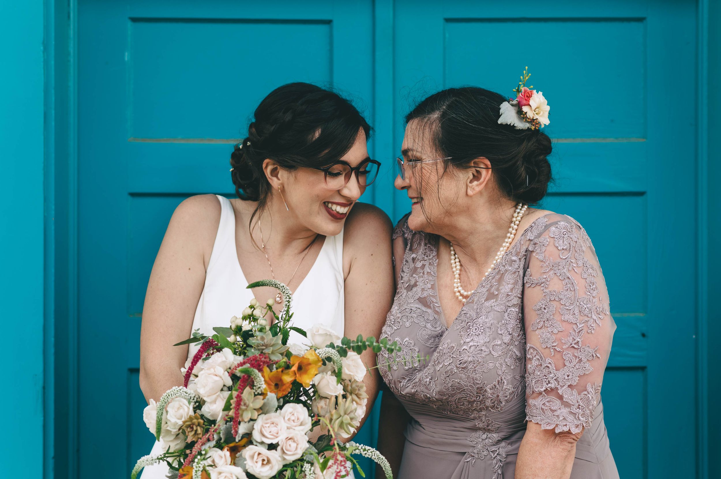 Bride giggling with her mother in front of blue door.