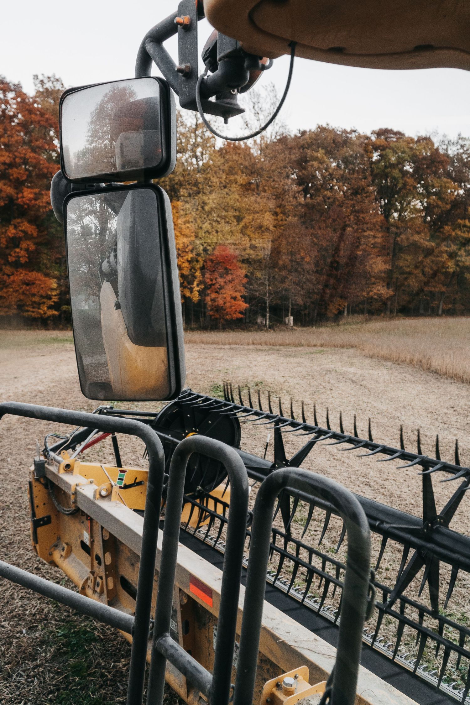 Side mirror view of farm equipment with fall foliage in background.
