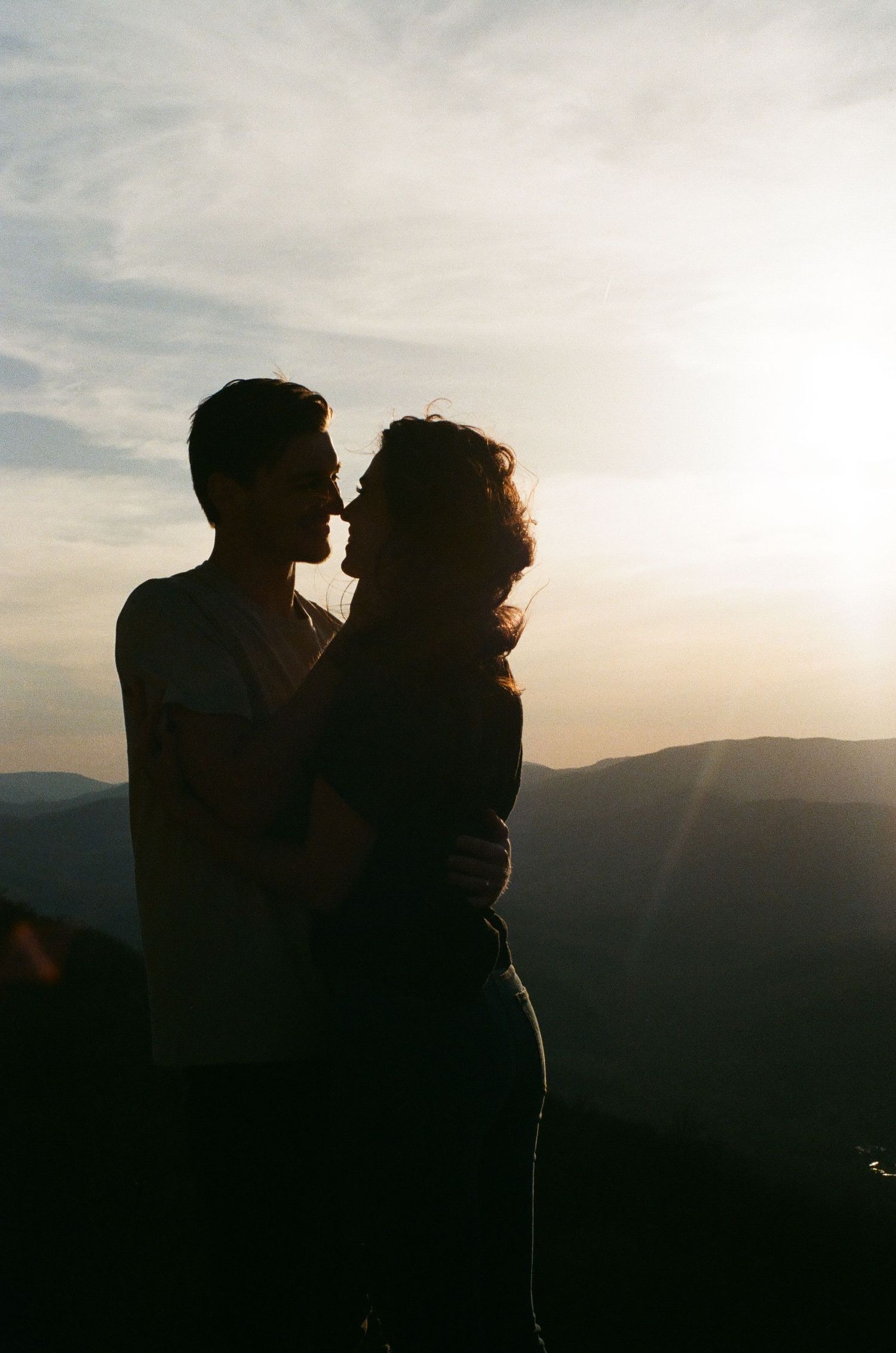 Silhouetted figures embrace against a backdrop of mountain ranges at sunset.