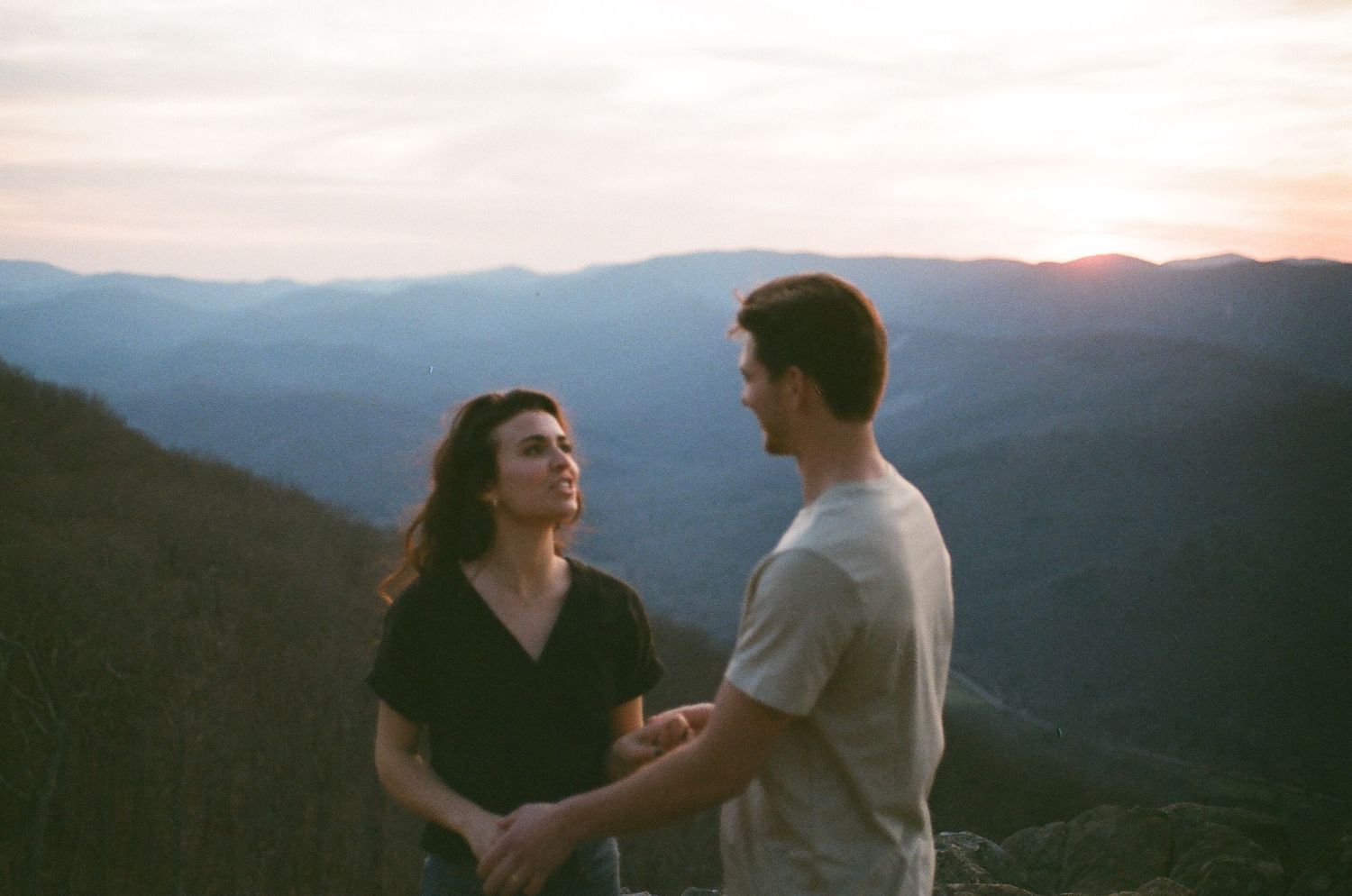Couple sharing a tender moment on a mountain summit during golden hour.