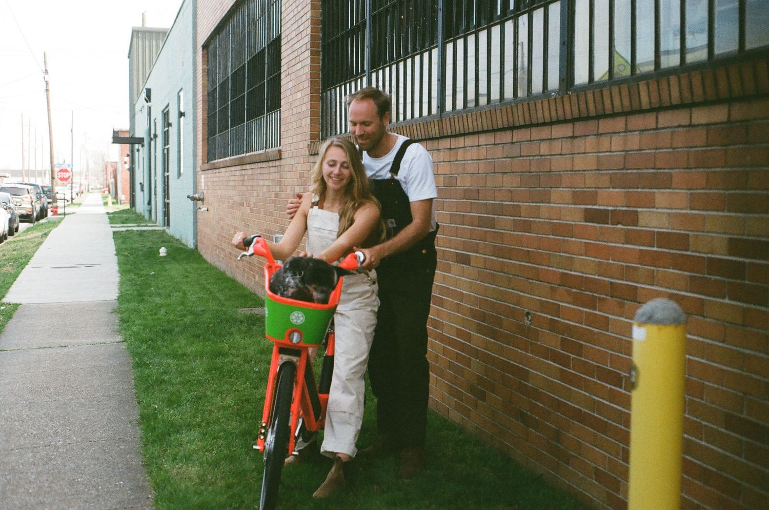 Teaching moment on a red bicycle against brick building with yellow safety pole.
