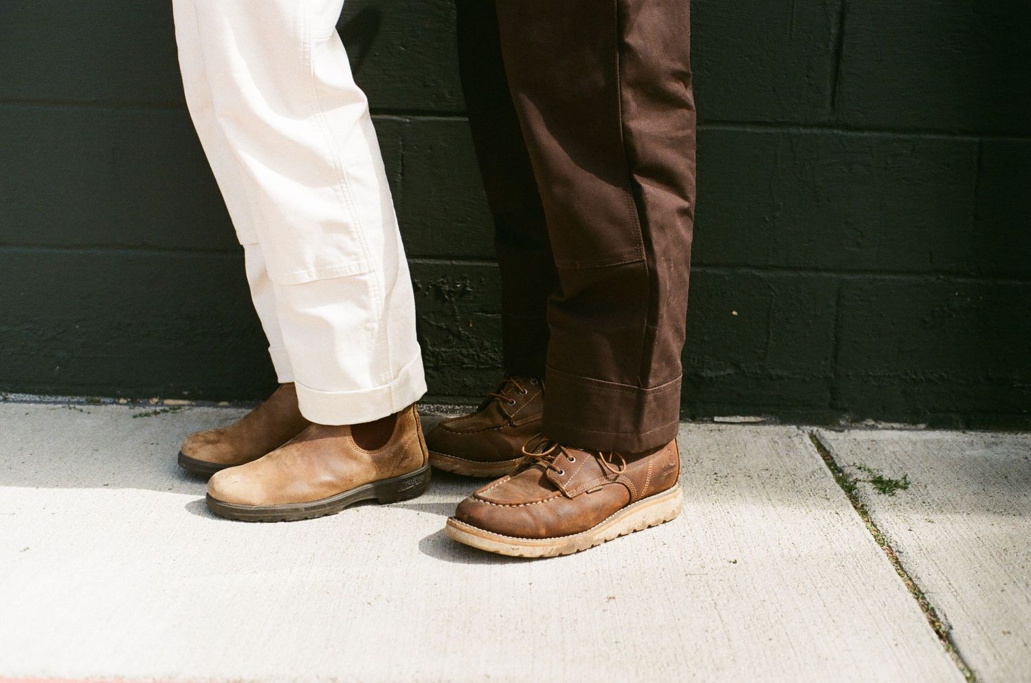 Close-up view of two pairs of brown leather dress shoes on a concrete sidewalk.
